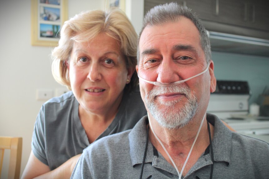 Blonde haired woman in grey shirt hovering over grey haired man with breathing tube