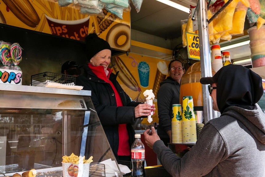 A woman serves an ice cream to a customer at a Dagwood Dog stall.