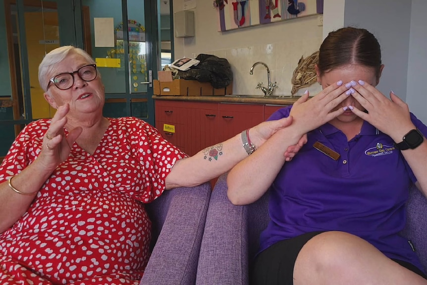 An older lady holds the arm of a young aged care worker holding hands over her face