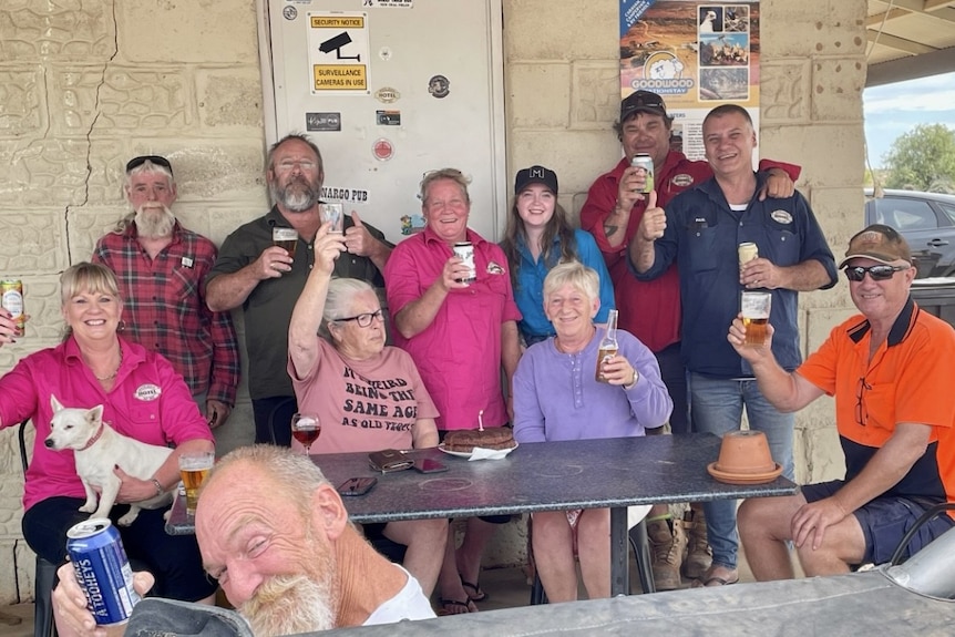 a group of people with beers in hand outside a rural pub 