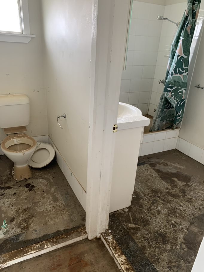 A bathroom which has previously flooded. Surfaces covered in dirt.