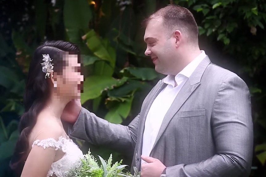 A man in a grey suit touches the face of a woman in a wedding dress. Her face is pixelated 