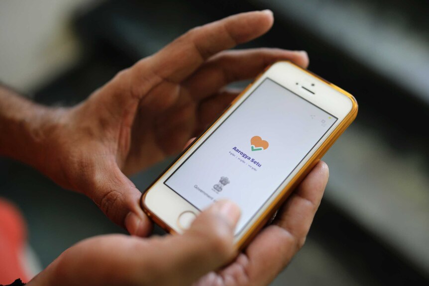 An iPhone is held in two hands, with the Aarogya Setu app on screen.