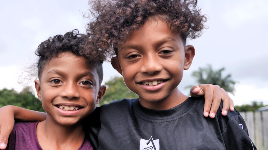Two young Indigenous twins with their arms around each other, smiling at the camera.