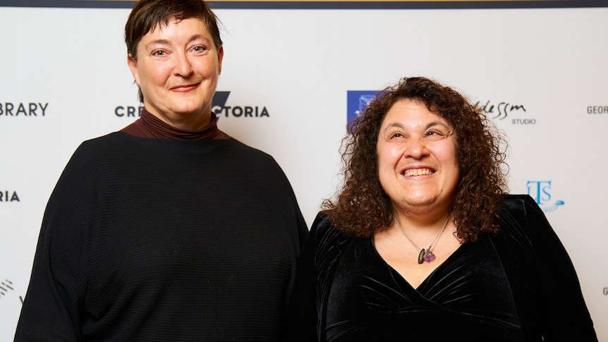 Marisa Sporsaro (right) and Leisa Shelton (left) smiling at the camera in front of a Victorian State Library Fellowship banner.