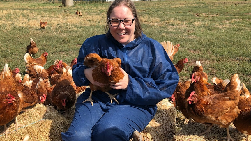 Melinda Hashimoto sitting with chickens while wearing personal protective gear.