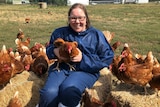Melinda Hashimoto sitting with chickens while wearing personal protective gear.