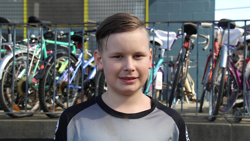 A boy stands in front of a row of bikes.