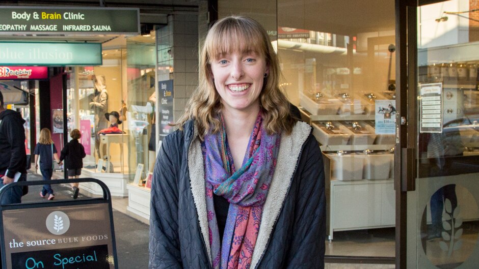 A woman stands on a street outside a wholefoods store.