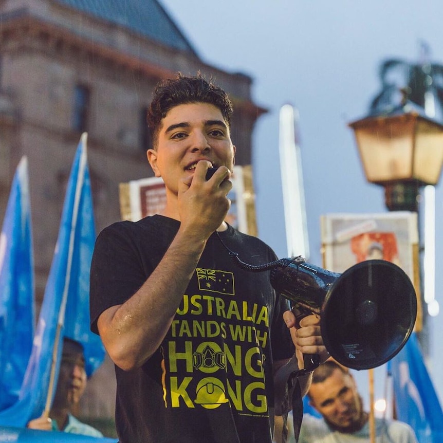 UQ philosophy student Drew Pavlou speaks at a rally with a megaphone.