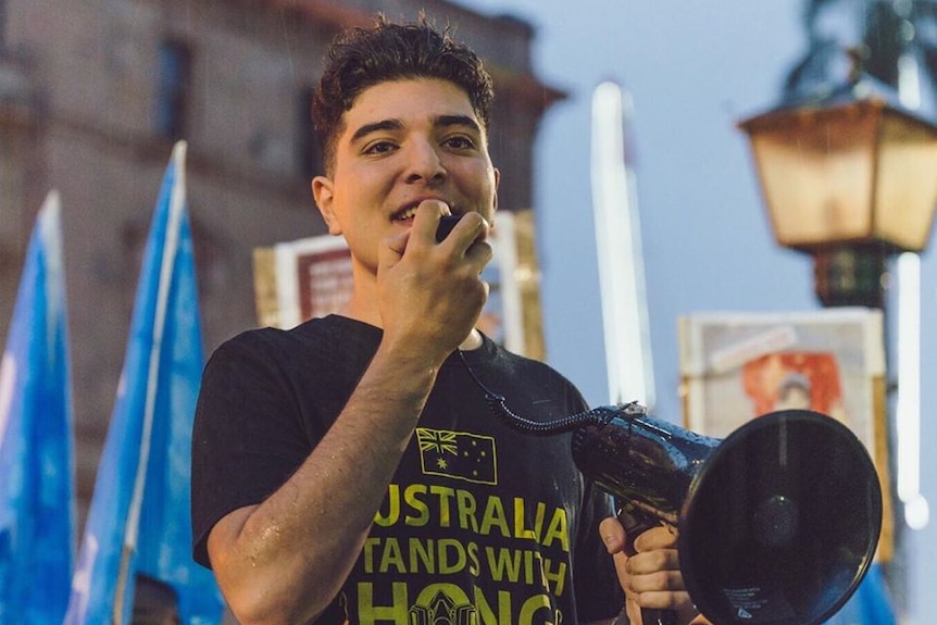 UQ philosophy student Drew Pavlou speaks at a rally with a megaphone.