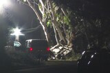 A night time scene of an overturned car by the side of the road with a van parked nearby.