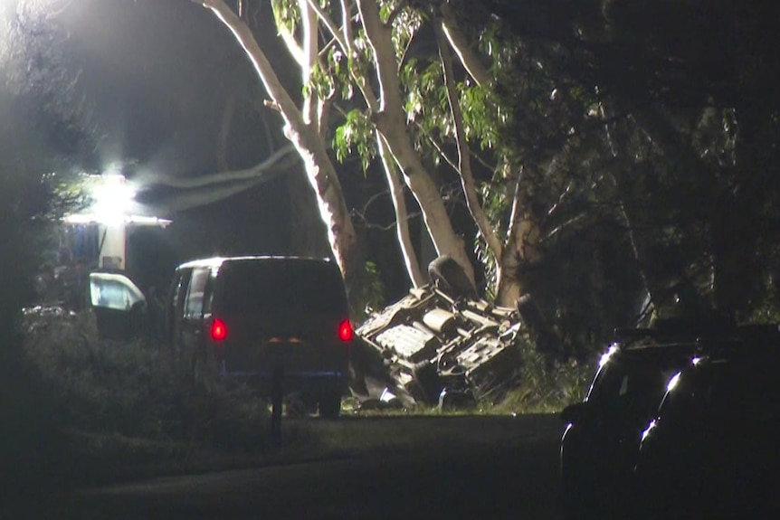 A night time scene of an overturned car by the side of the road with a van parked nearby.