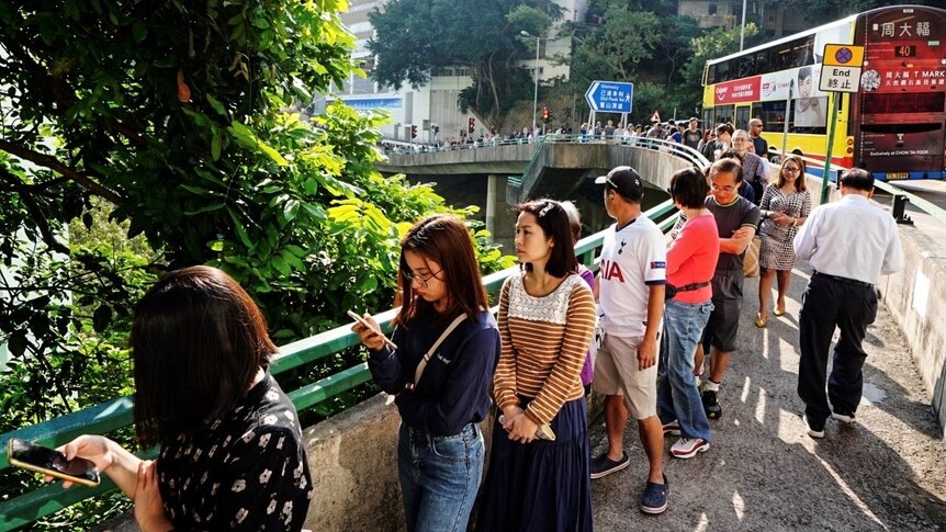 A long queue of people stretches down a pathway on a main road as they wait to vote in Hong Kong.