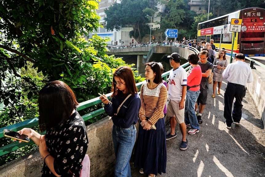 A long queue of people stretches down a pathway on a main road as they wait to vote in Hong Kong.