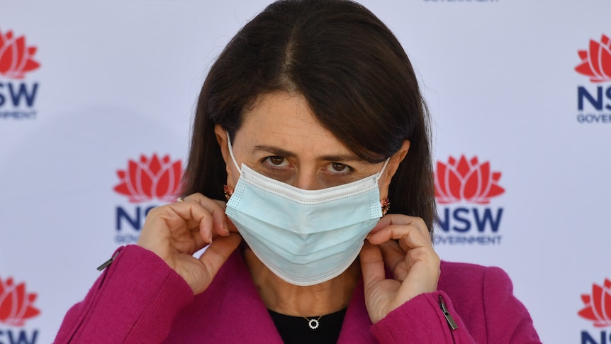 Gladys Berejiklian adjusts her mask as she looks up.