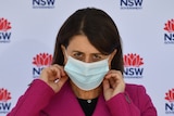 Gladys Berejiklian adjusts her mask as she looks up.