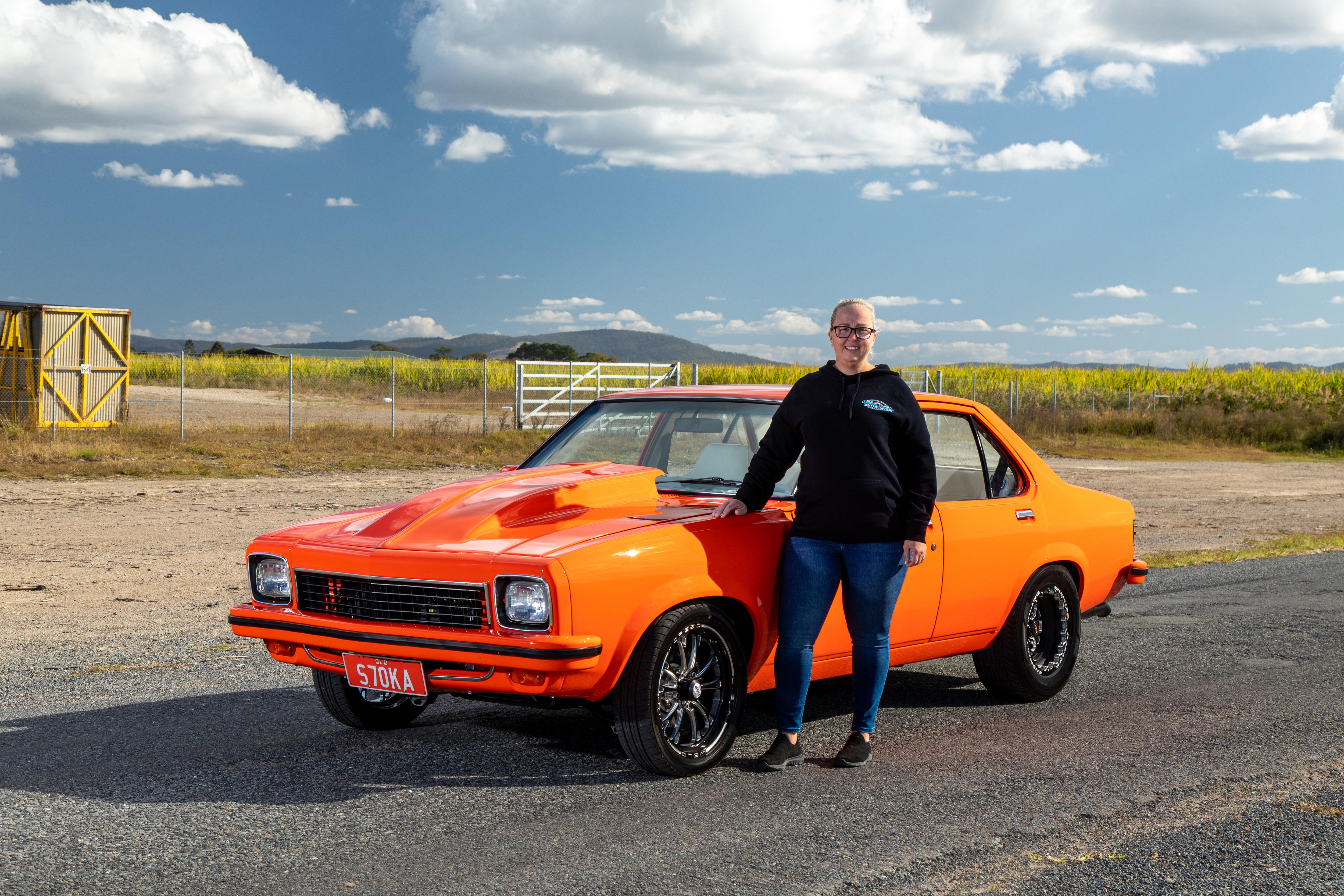 Una mujer se encuentra junto a un automóvil Torana de color naranja brillante.