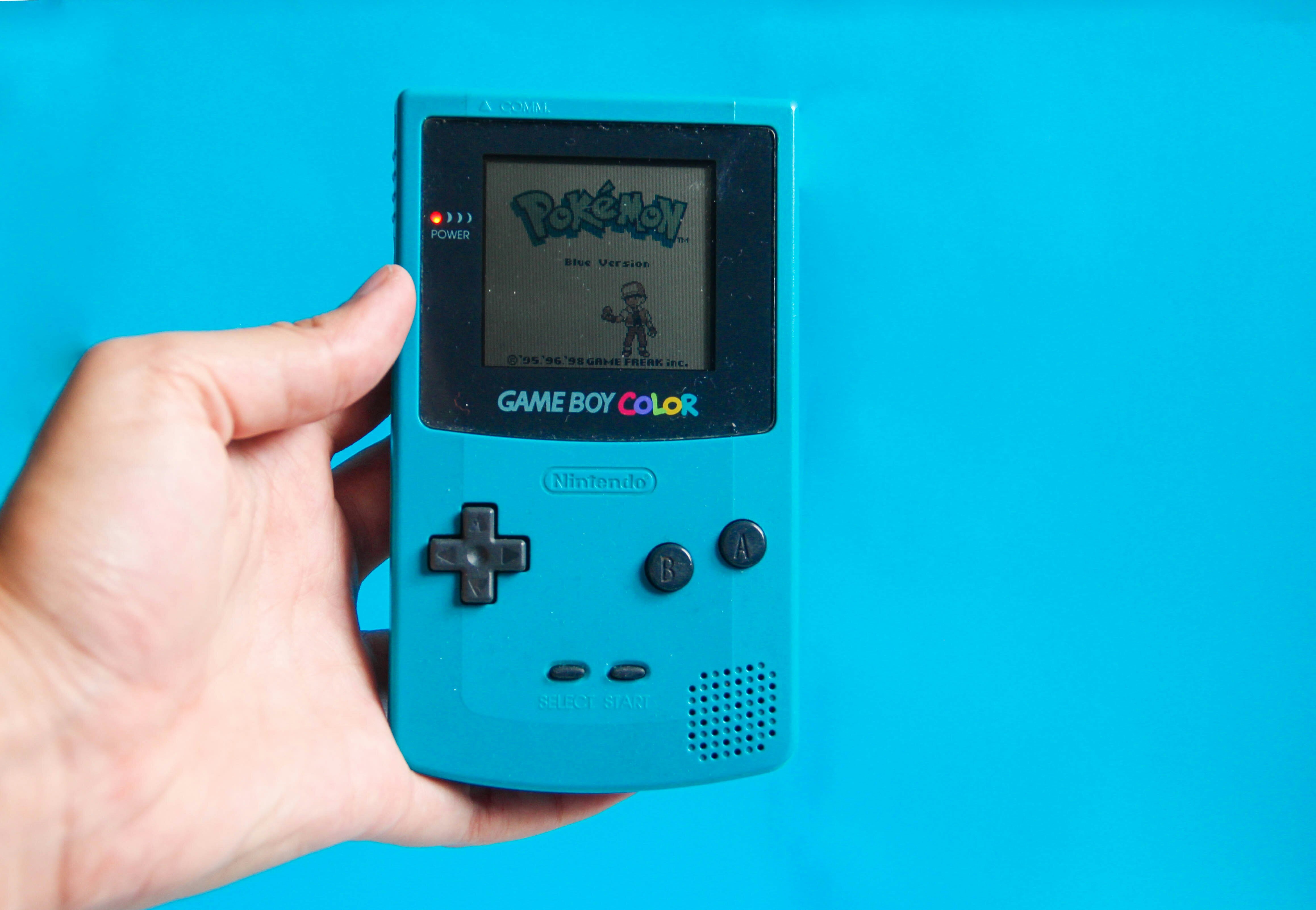 A hand holding a Gameboy Colour with Pokemon on it