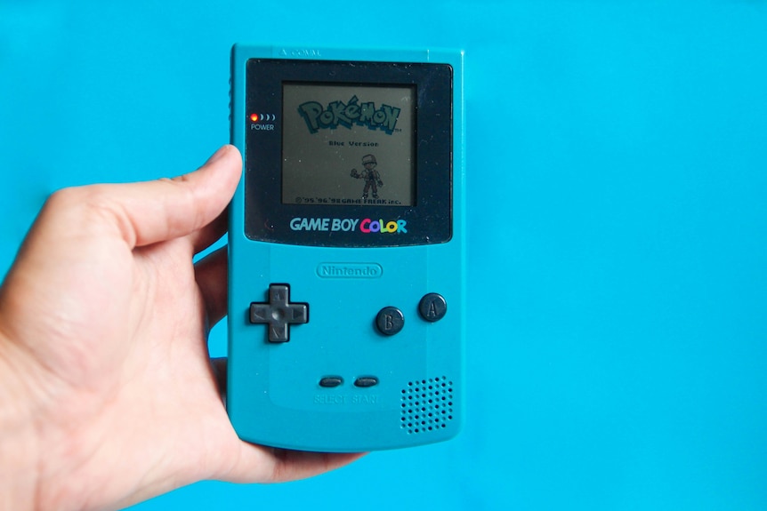 A hand holding a Gameboy Colour with Pokemon on it