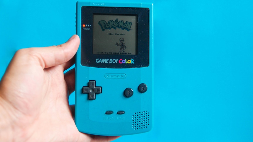 A hand holding a Gameboy Colour with Pokemon on it