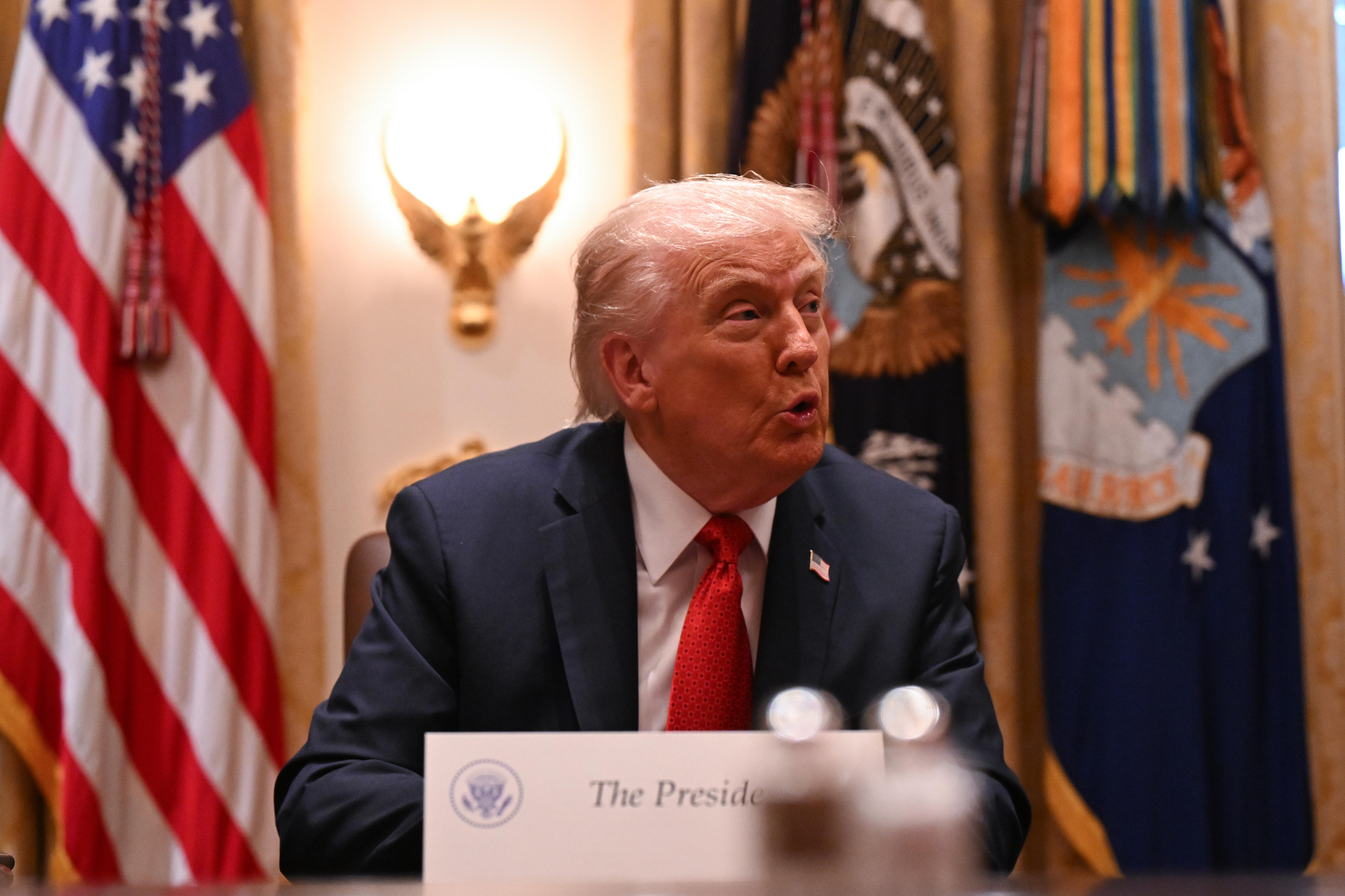 Trump sits a table behind a placard with his title.