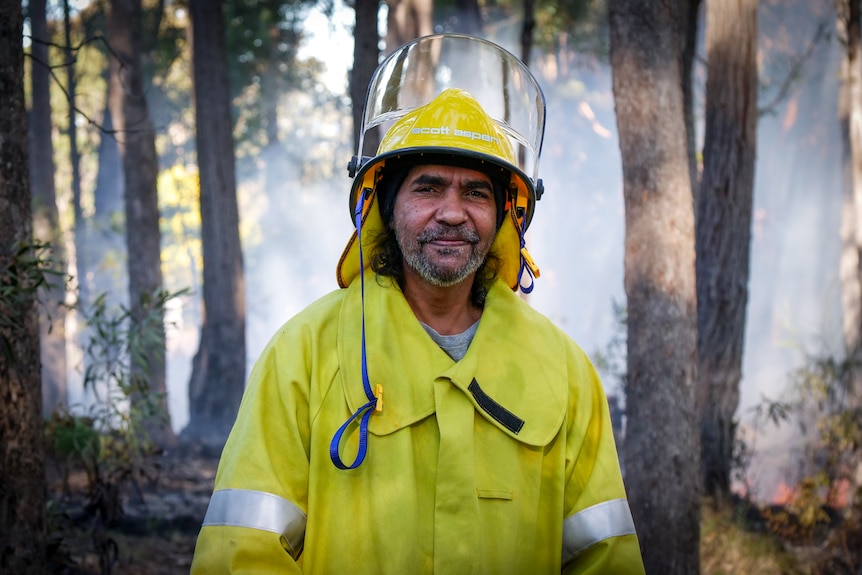 Portrait of man in yellow firefighting jacket and helmet, smiling.
