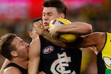 Sam Walsh grimaces as two Richmond players tackle him. He is trying to get the ball free