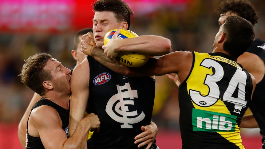 Sam Walsh grimaces as two Richmond players tackle him. He is trying to get the ball free