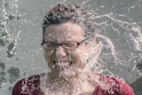 A headshot of a woman screwing up her face as it is splashed with water.