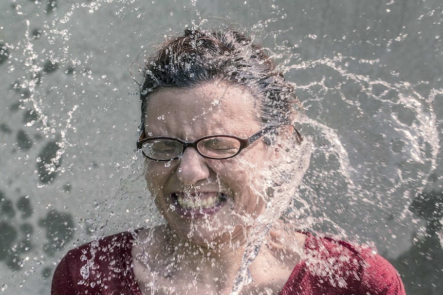 A headshot of a woman screwing up her face as it is splashed with water.