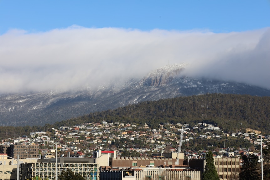 A snow-dusted mountain with city buildings and houses in the foreground