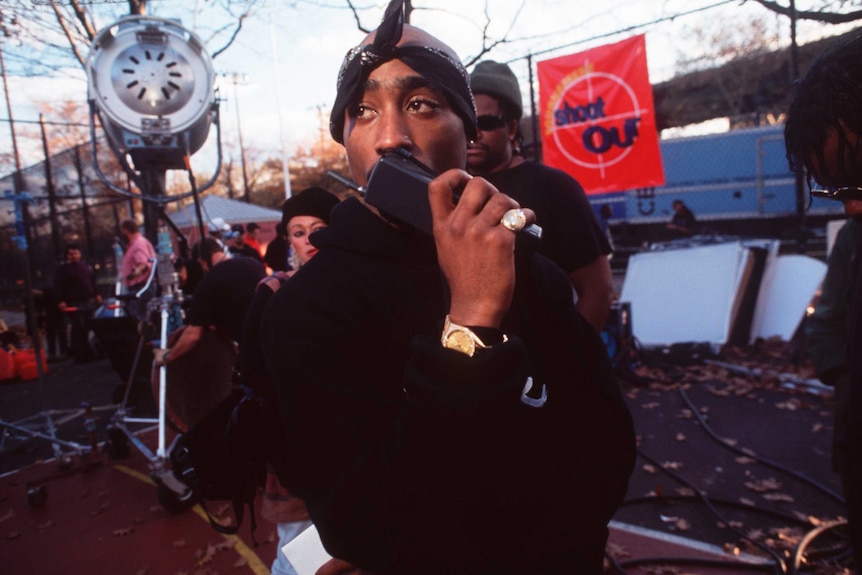 Rapper Tupac Shakur, a young African American man in a hoodie, speaks into a walkie talkie on a film set