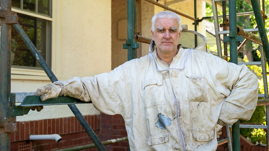 Man wearing a beekeeping top standing beside scaffolding. 