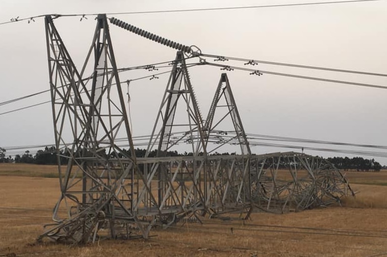 A power transmission tower lies collapsed on a field.