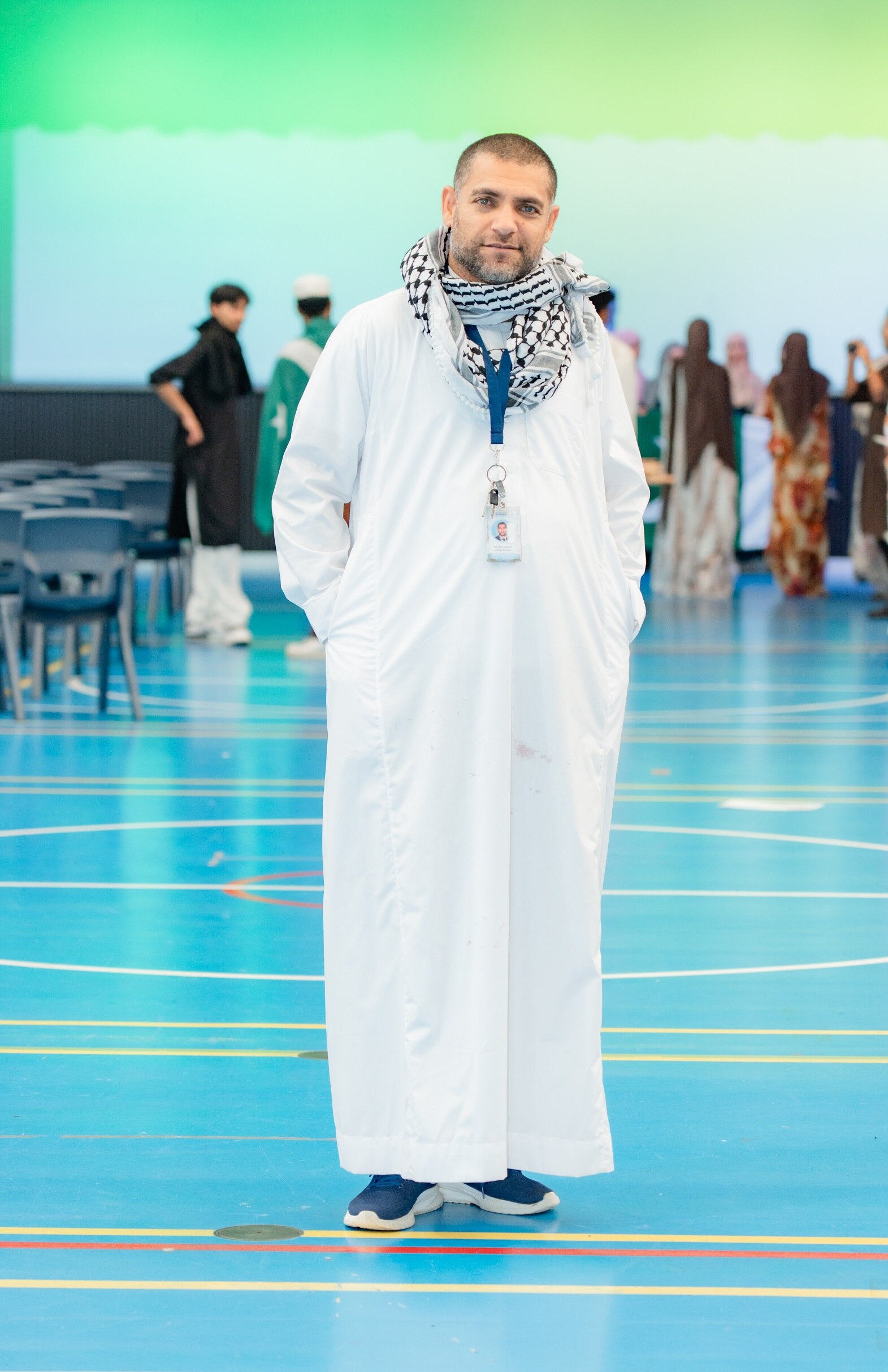 Sami Muamar is wearing traditional dress and standing in a function room with others in the background.