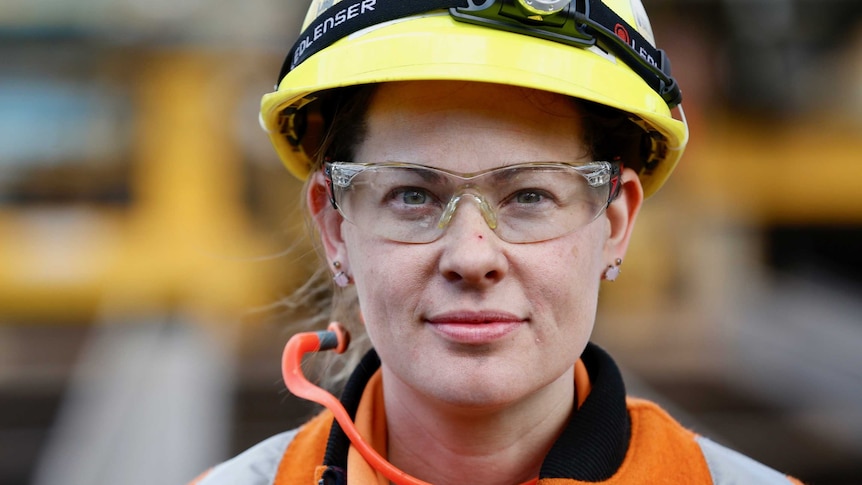 A woman in high vis clothing, protective hard hat and goggles looks straight ahead