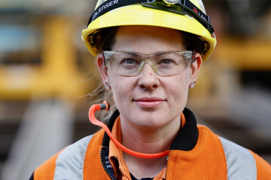 A woman in high vis clothing, protective hard hat and goggles looks straight ahead