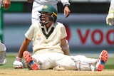 Australia batsman Joe Burns sits on the floor, surrounded by Indian fielders during a Test at the MCG.