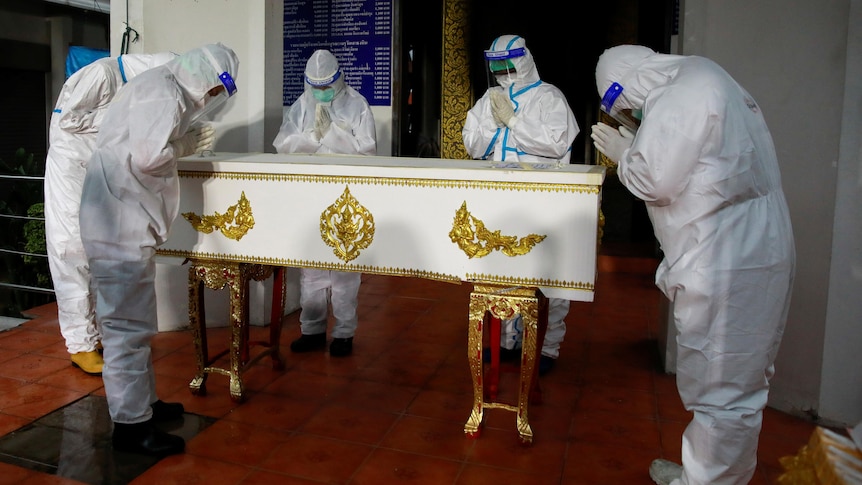 A group of people in full PPE bow to a coffin 