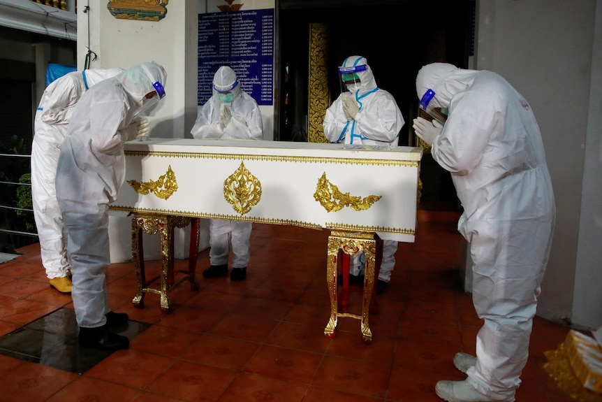 A group of people in full PPE bow to a coffin 