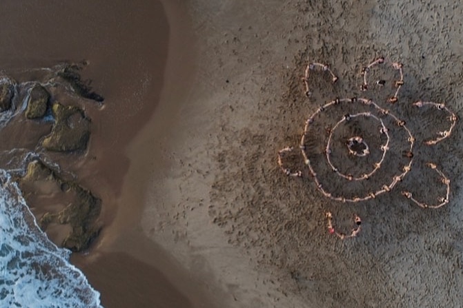 A drone shot of women lying in a women's meeting place symbol, created by local Indigenous women, for a beach photoshoot