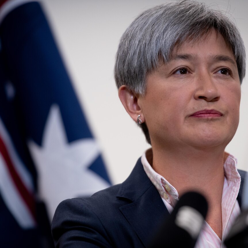 Penny Wong at a press conference standing in front of an Australian flag. 