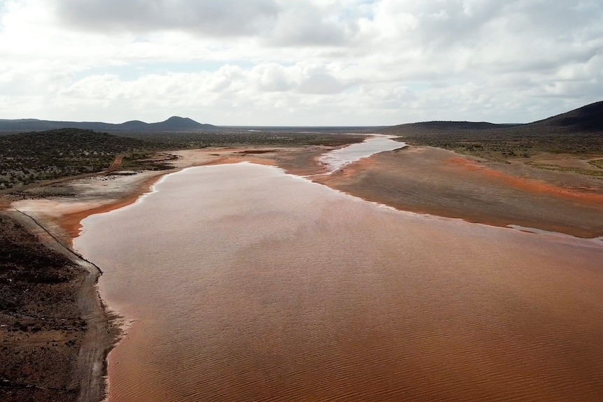 A drone shot of brown inland lake stretching to hills on the horizon.