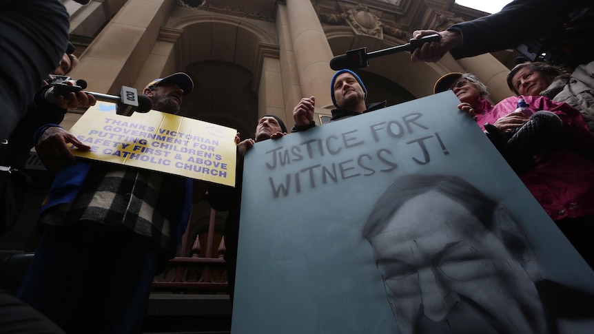 Protestors holding signs outside the court building, one says "justice for witness j!"