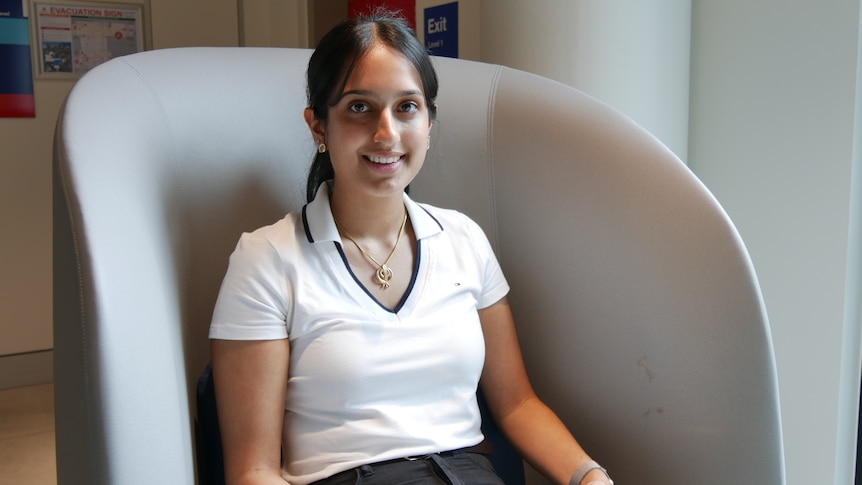 Bavelin sitting in a large chair, smiling and holding a notebook.