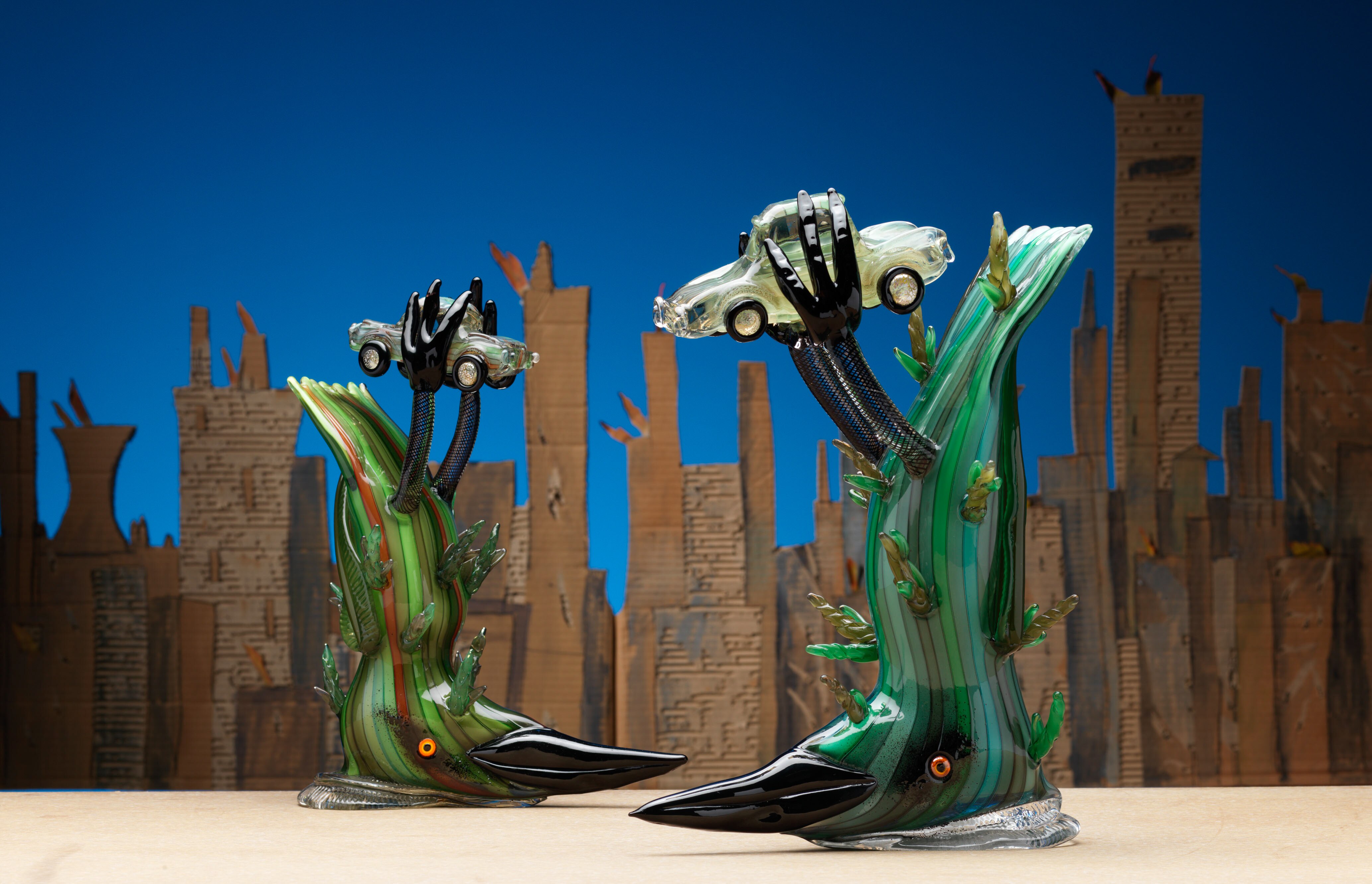 Two glass sculptures by artist Tom Moore - of birds on their backs holding small cars between their feet