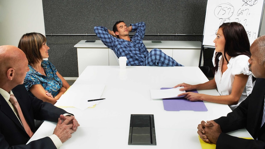 5 people sitting around a work table. one man is leaning back with his eyes closed while wearing pyjamas