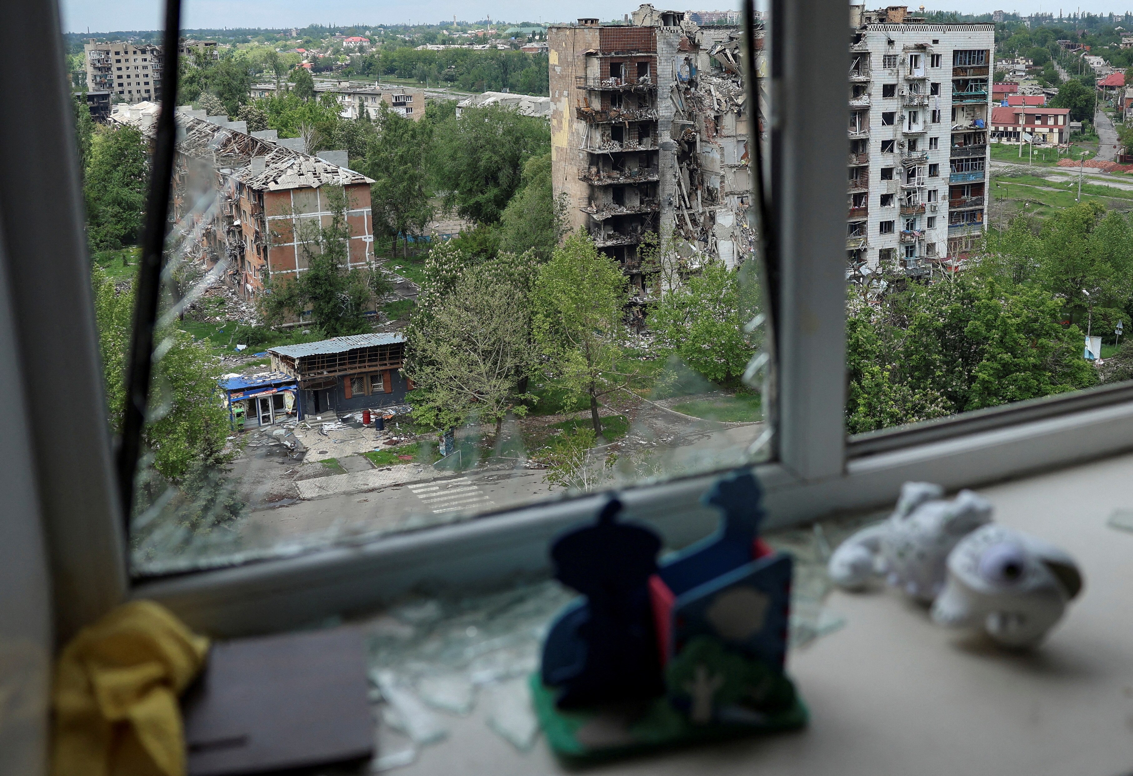 A view of damaged apartment buildings in a Ukrainian city seen through a smashed glass window.