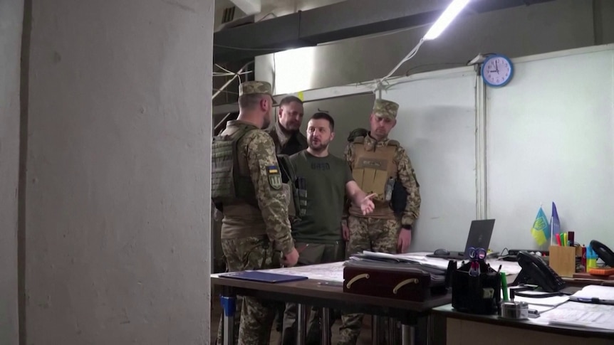 Volodymyr Zelenskyy examines documents with men in army uniforms. 